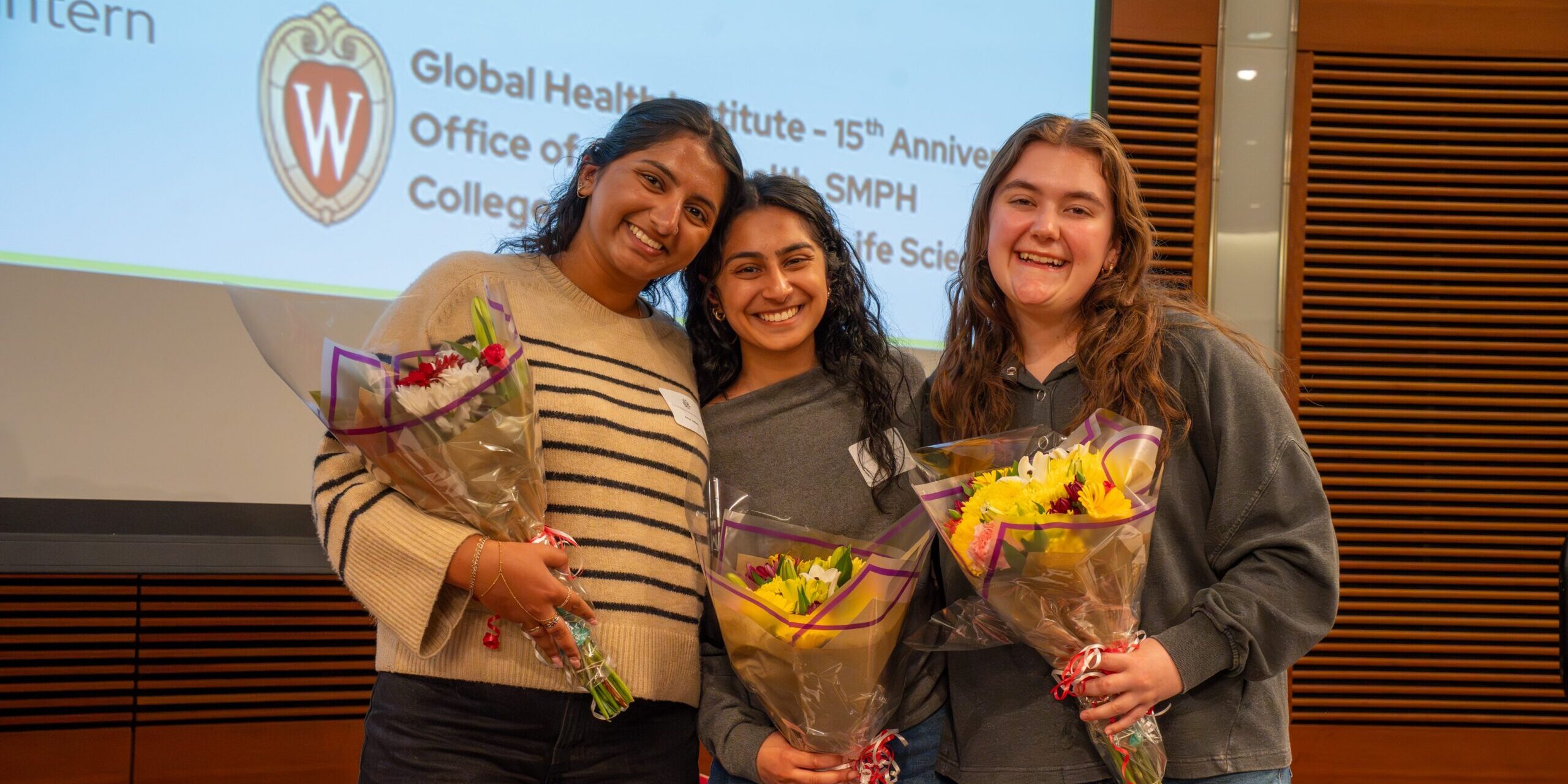 Three Global Health Institute students each holding a bouquet of flowers.